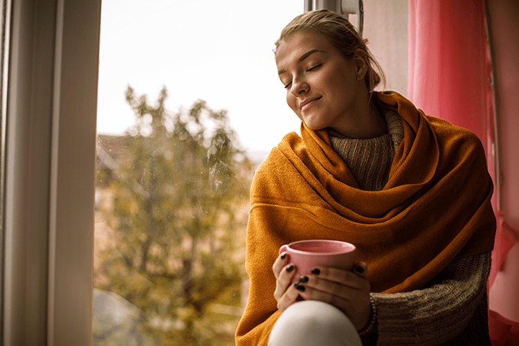 woman in fall with cup of coffee next to the window.